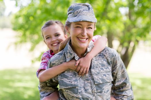 Happy female soldier giving a piggyback ride to her daughter in park