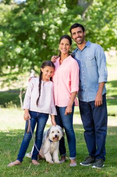 Portrait of happy family with their pet dog standing in park on a sunny day