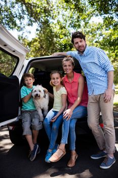 Portrait of happy family sitting in car trunk with their dog