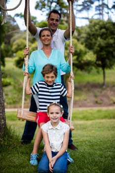 Portrait of happy family sitting on a swing in park on sunny a day