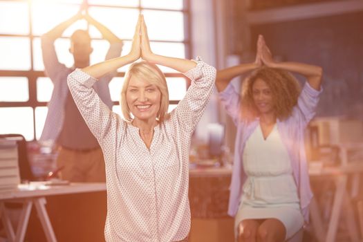 Portrait of happy businesswoman practicing yoga with coworkers in creative office
