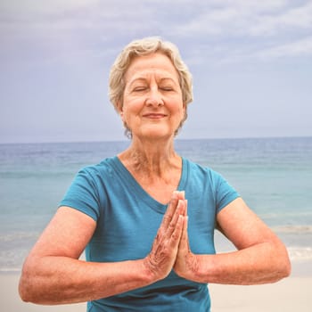 Happy senior woman in lotus position on the beach