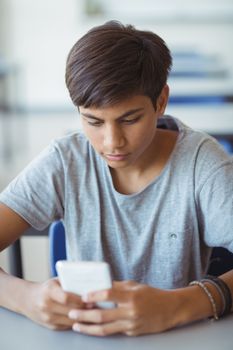 Schoolboy using mobile phone in classroom at school