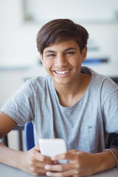 Portrait of happy schoolboy using mobile phone in classroom at school