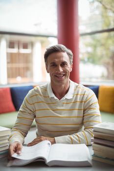 Portrait of happy school teacher reading book in library at school