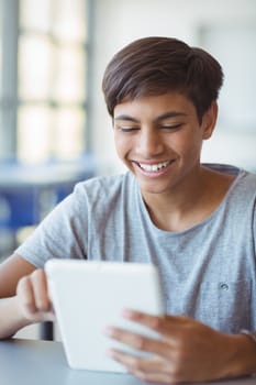 Happy schoolboy using digital tablet in classroom at school