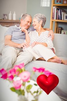 red heart against happy romantic senior couple sitting on sofa 3d