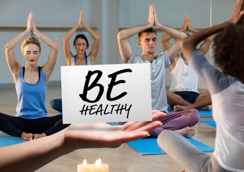 Digital composition of hand holding card with text be healthy in yoga class