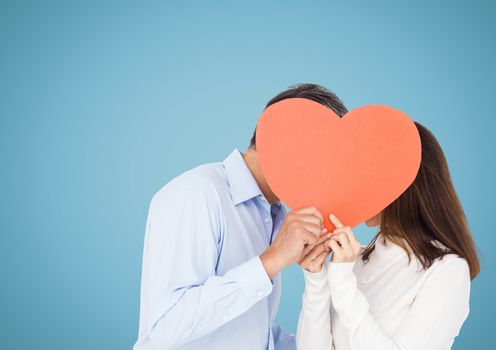 Romantic couple holding heart shape and kissing each other against blue background