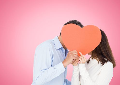 Romantic couple holding heart shape and kissing each other against pink background