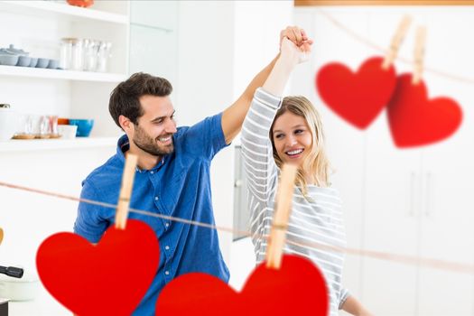 Composite image of red hanging hearts and romantic couple dancing at home