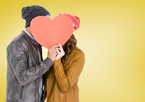 Romantic couple holding heart shape and kissing each other against yellow background