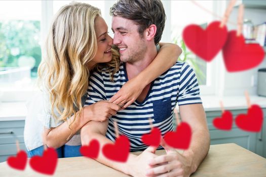 Composite image of red hanging hearts and romantic couple smiling in kitchen