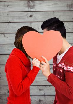 Romantic couple hiding their face behind heart against wooden background