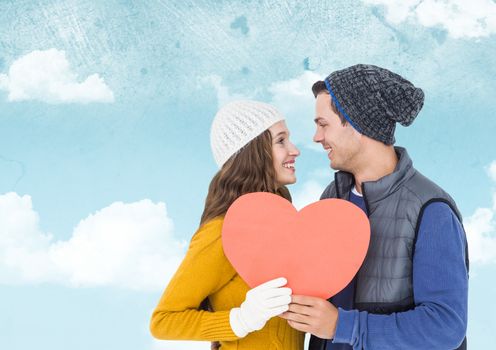 Composite image of romantic couple holding heart shape against sky
