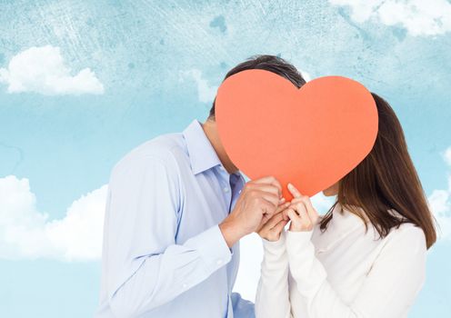 Romantic couple hiding their face behind heart against sky