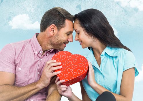 Romantic couple holding a heart shaped box against sky