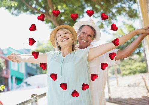 Portrait of romantic couple standing with arms outstretched with digitally generated of heart