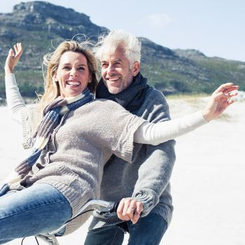 Carefree couple going on a bike ride on the beach on a bright but cool day