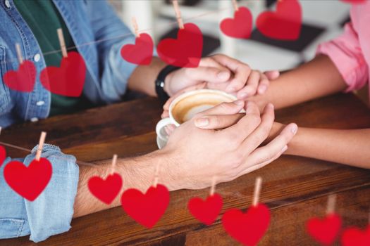 Mid section of romantic couple holding hands while having coffee