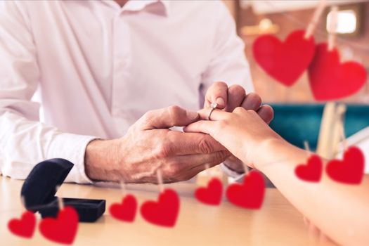 Composite image of romantic couple exchanging rings with red hearts hanging on line