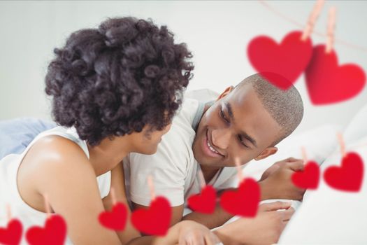 Composite image of red hearts and romantic couple lying on bed in bedroom at home