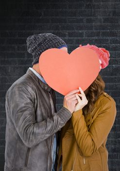 Romantic couple hiding their face behind red heart against brick background