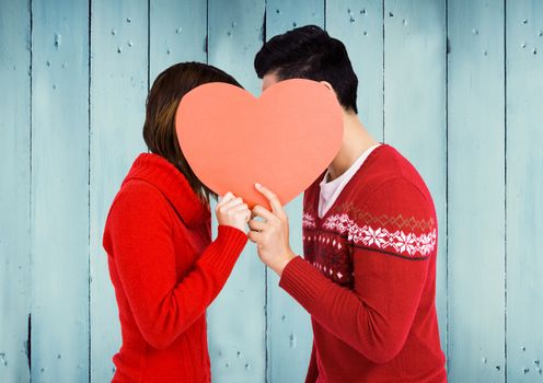 Romantic couple hiding their face behind heart against wooden background