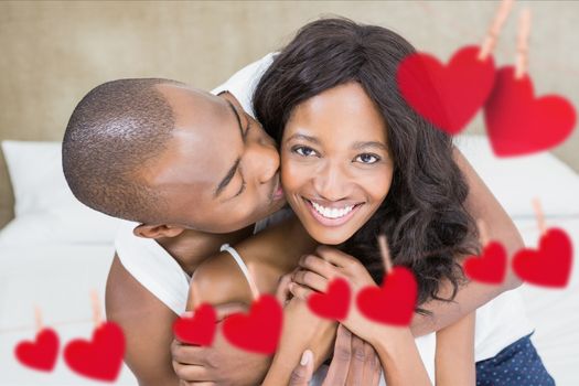 Composite image of romantic couple on bed in bedroom with red hearts hanging on line