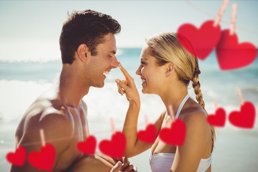 Composite image of romantic couple enjoying on the beach with red hearts hanging on line