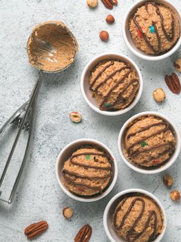 Safe-to-eat raw monster cookie dough in small portion bowl, ice cream scoop and nuts on gray cement background. Ideas and recipes for kids and toddlers meal. Top view or flat-lay