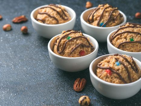 Safe-to-eat raw monster cookie dough in small portion bowl and nuts on dark blue background. Ideas and recipes for kids and toddlers meal. Copy space for text.