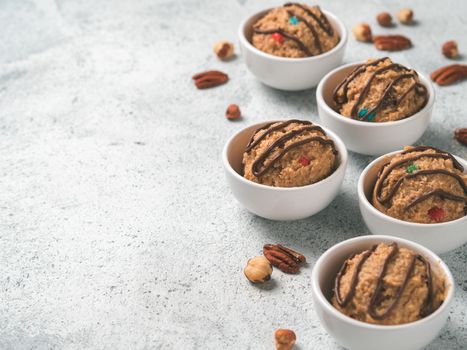 Safe-to-eat raw monster cookie dough in small portion bowl and nuts on gray cement background. Ideas and recipes for kids and toddlers meal. Copy space for text.