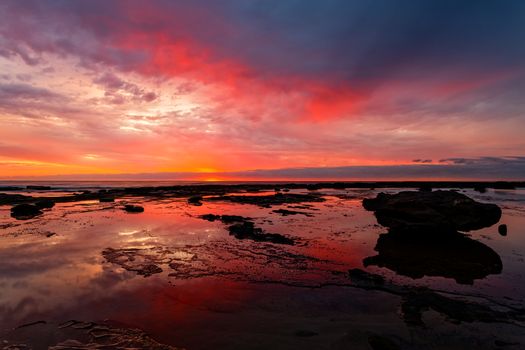 Sunrise coastal seascape at low tide with vivid cloud reflections