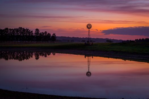 Pretty dawn sky over dam with wind mill in rural Australia.  Reflections of sky in water