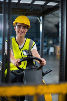 Portrait of smiling female factory worker driving forklift in factory