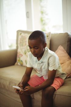 Boy sitting on sofa and using mobile phone in living room at home