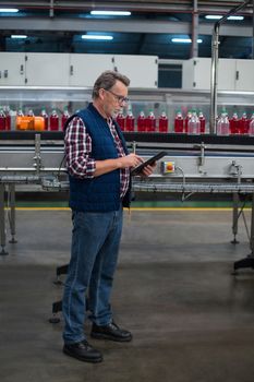 Factory worker using digital tablet next to production line in drinks production plant