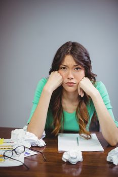 Frustrated female business executive sitting with crumpled paper balls in office