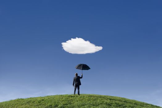 Businessman on a hill holding umbrella underneath a single cloud themes of anticipation protection out of context