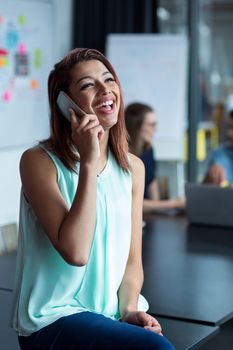 Smiling female business executive talking on mobile phone in office