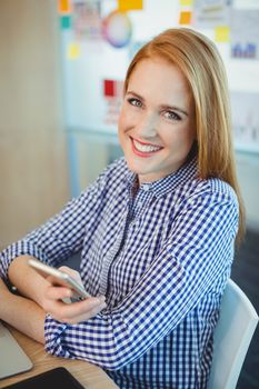 Portrait of female graphic designer holding mobile phone in office