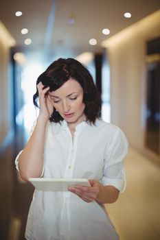 Female business executive using digital tablet in corridor at office