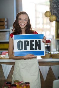 Female shop assistant holding open sign board at grocery shop