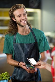 Smiling male staff receiving a payment through nfc technology at counter in shop