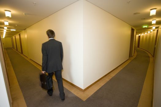 A businessman looking down the corridoor of a hotel themes of travel working late arrival