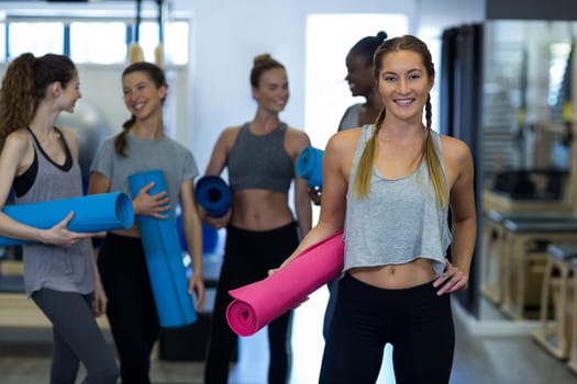 Portrait of beautiful woman holding yoga mat in gym