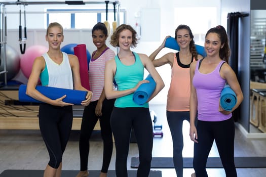 Portrait of beautiful women holding yoga mat in gym