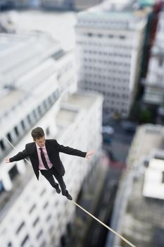 Businessman walking on a tightrope across buildings themes of agility balance