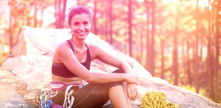 Woman smiling and sitting on a rock with climbing equipment 